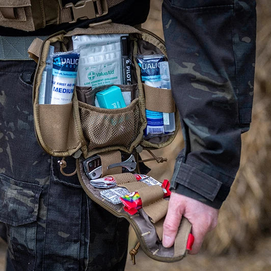 Person wearing a tactical vest with a utility pouch containing various items.