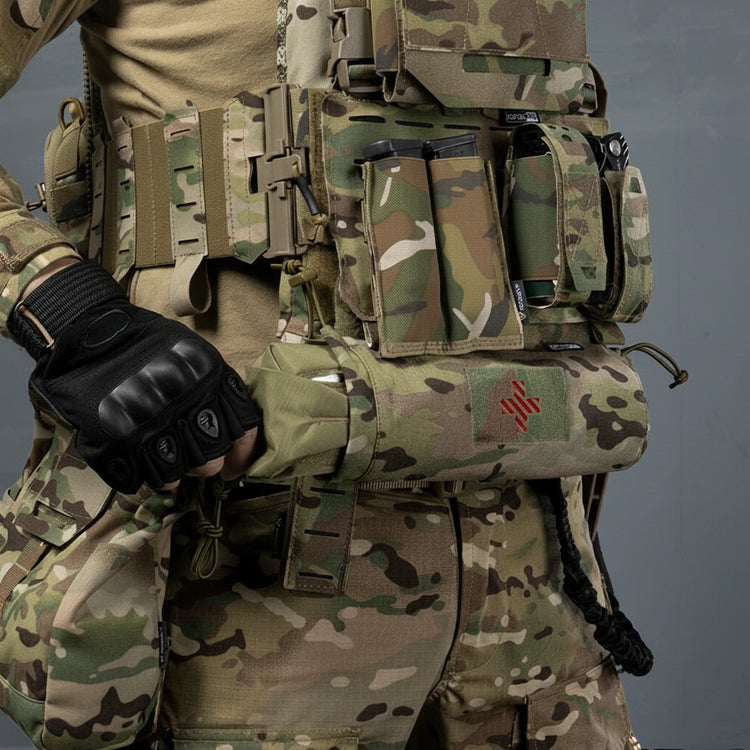 Person wearing a camouflage tactical vest with multiple pouches and a gloved hand, on a gray background.