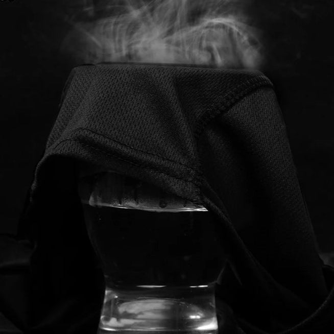 Black face mask draped over a glass container with smoke rising against a dark background