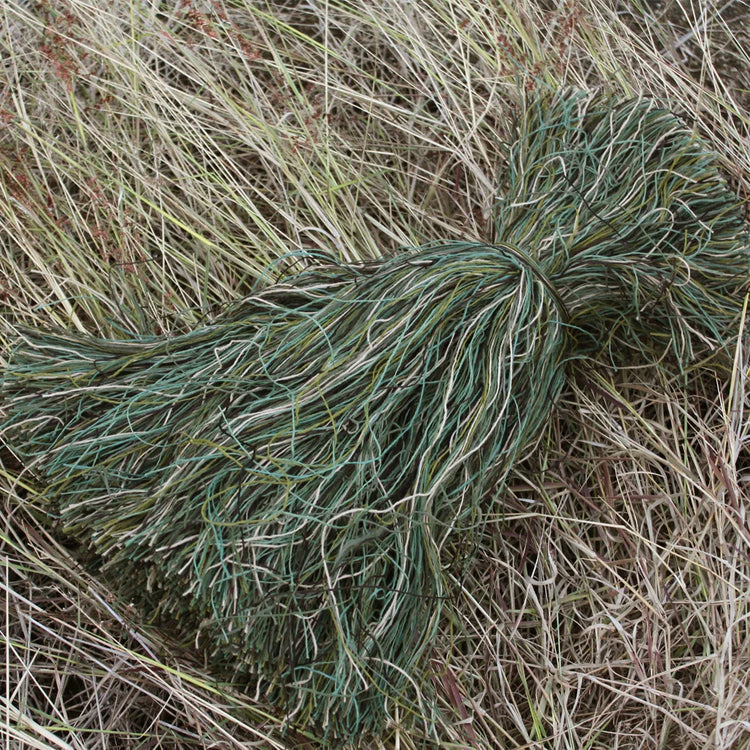 Close-up of green Ghillie Burlap Yarn Hessian Twine Jute tuft among brown grasses