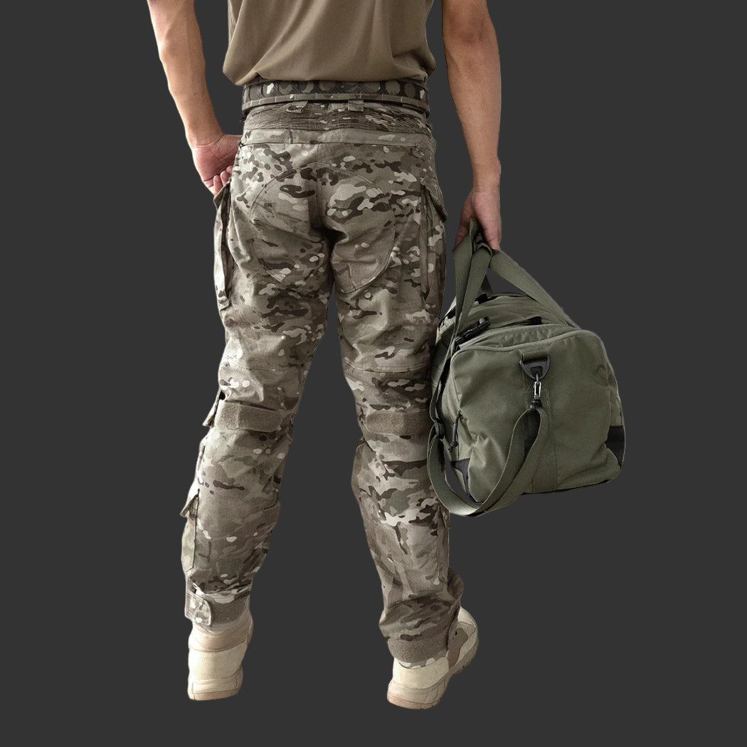 Person wearing camouflage pants and holding a green duffel bag against a neutral background