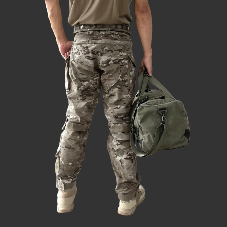 Person wearing camouflage pants and holding a green duffel bag against a neutral background